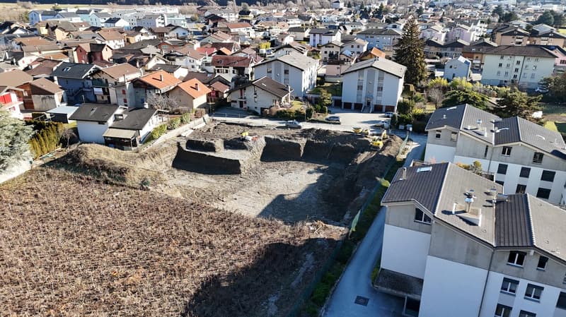 Aerial view of a residential neighborhood, showing various houses, one under construction, and a plot of land in progress.