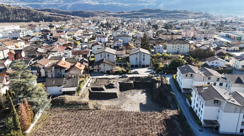 Aerial view of a town with many houses, some under construction, surrounded by trees and mountains