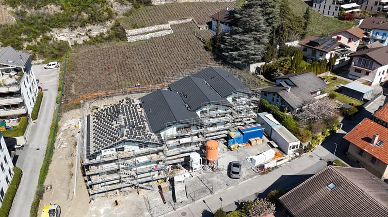 House under construction, multiple floors, solar panels on the roof, scaffolding, cars parked in the area
