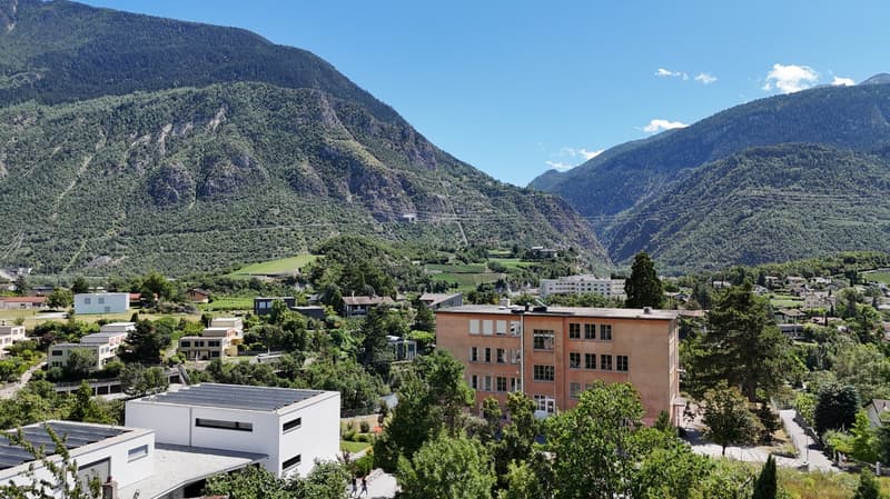 Aerial view of a neighborhood with buildings, trees, mountains, and clear blue sky.