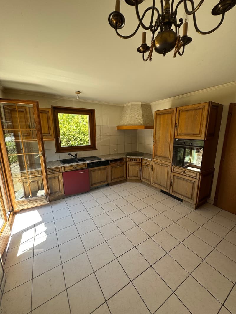 Open-plan kitchen, wooden cabinets, granite countertop, stainless steel sink, built-in dishwasher, oven, dishwasher, chandelier, double doors leading to a patio, window with a view.