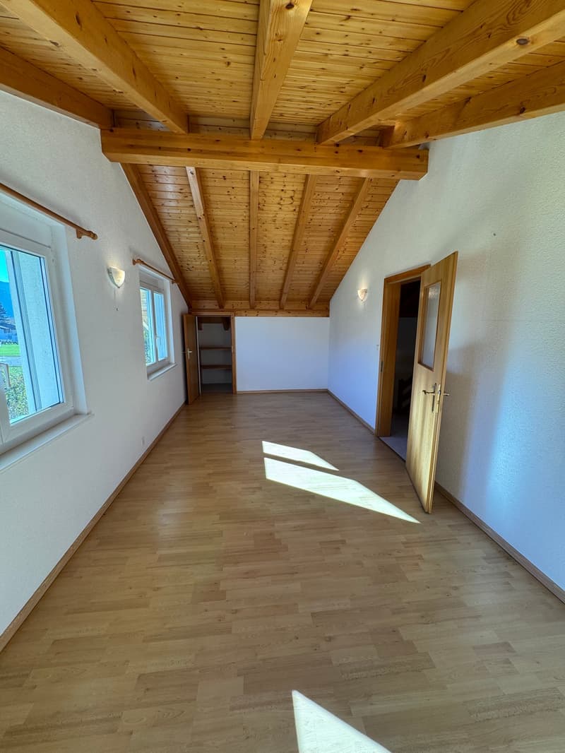 a bright room with a wooden ceiling, white walls, and wooden floors. It has windows and a wardrobe.