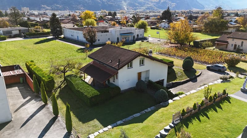 A small house with a brown roof, one garage, one car parked on the driveway.