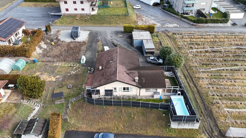 House with brown roof, solar panels, swimming pool, car parked outside, small garden, surrounded by a fence