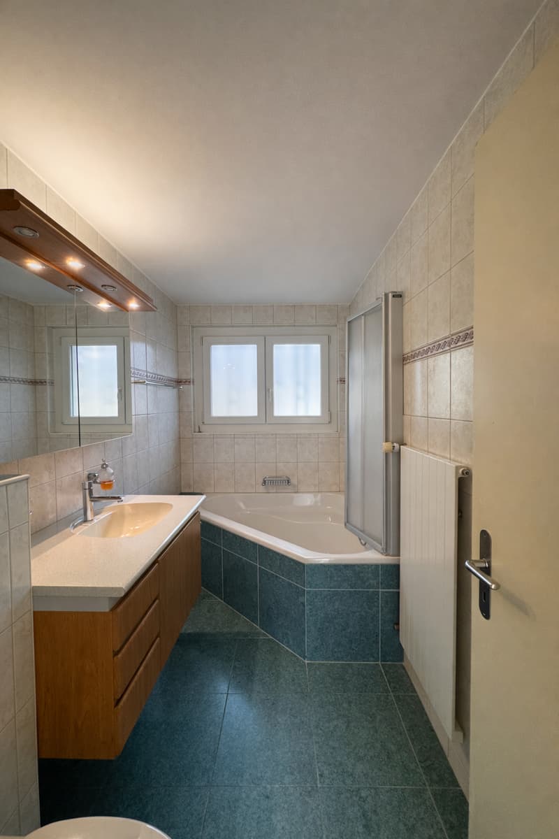Bathroom: blue tiled floor, large mirror, wooden cabinets, white sink, white bathtub, shower enclosure, radiator