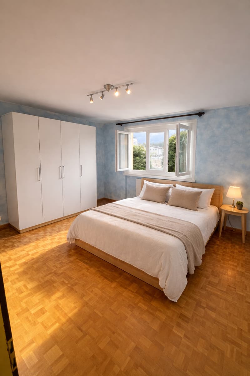 modern bedroom, blue walls, white wardrobe, double bed with pillows, nightstand with lamp and plant, wooden floor, ceiling light fixture, window with views
