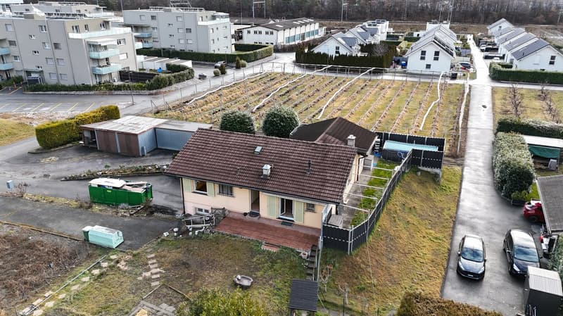 Single family house, brown roof, beige walls, entrance gate, car parking, paved driveway, neighboring houses, shrubs, fenced garden, shed