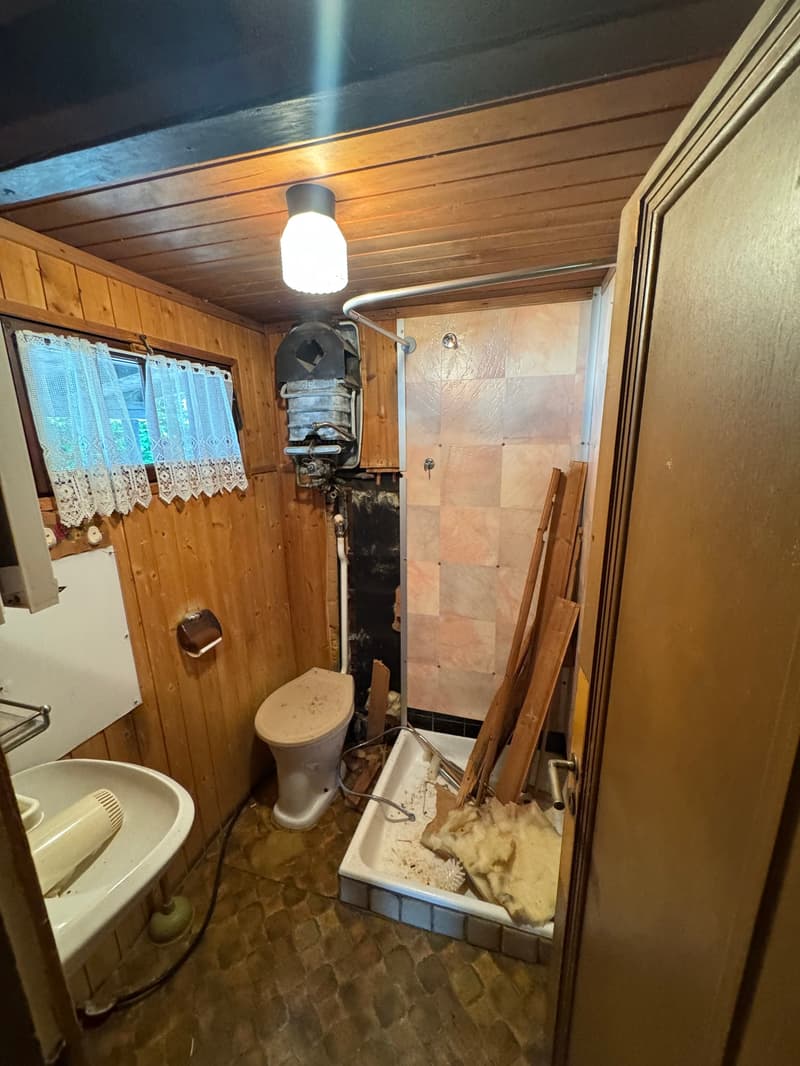 Small bathroom with wooden walls and ceiling, tiled floor, toilet, sink, and a washing machine visible.