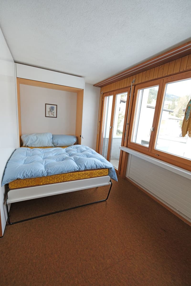 Single bed with blue bedding, glass doors to balcony, wooden wall panels, window, framed artwork