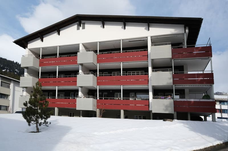 Multiple floor building with white walls, red balconies and snow on the ground