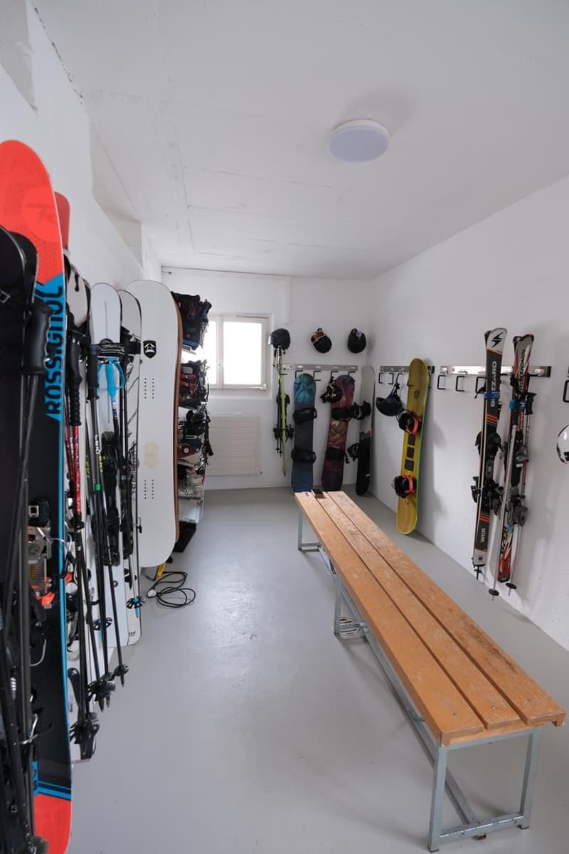 Room full of snowboards, skis, poles, and helmets, bench in the middle