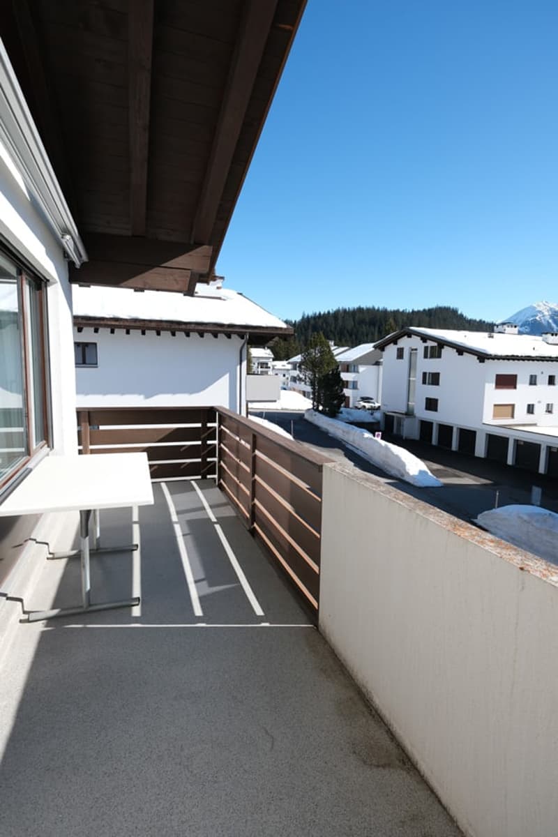 Balcony with wooden railing, table, and a view of the snowy mountains