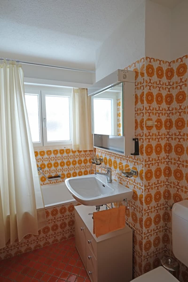 Bathroom with white sink, mirror, bathtub, and orange and white tiles
