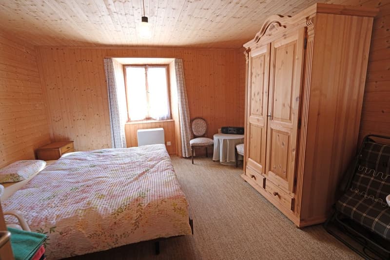 bedroom with wooden walls, bed, chair, table, wardrobe, window