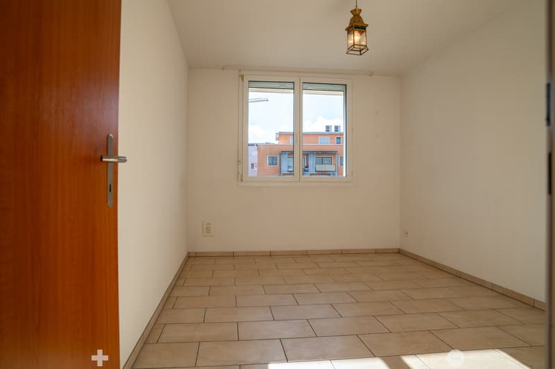 Empty room, beige tiles, white walls, large window with city view, ceiling lamp
