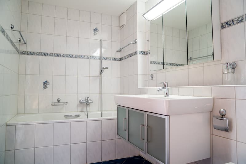 white tiles, bathtub, shower, mirror, sink, faucet, cabinet, soap dispenser, white walls