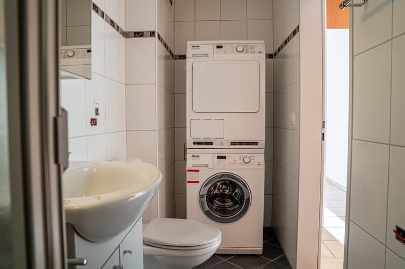 Bathroom with white tiles, white washing machine, white dryer, white toilet, white sink