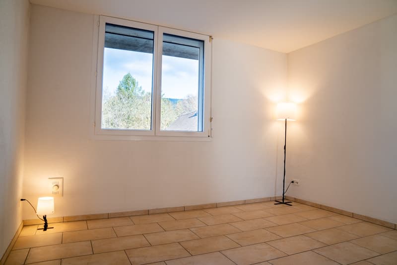 empty room with white walls, beige tiles, floor lamp, wall lamp, window with trees outside