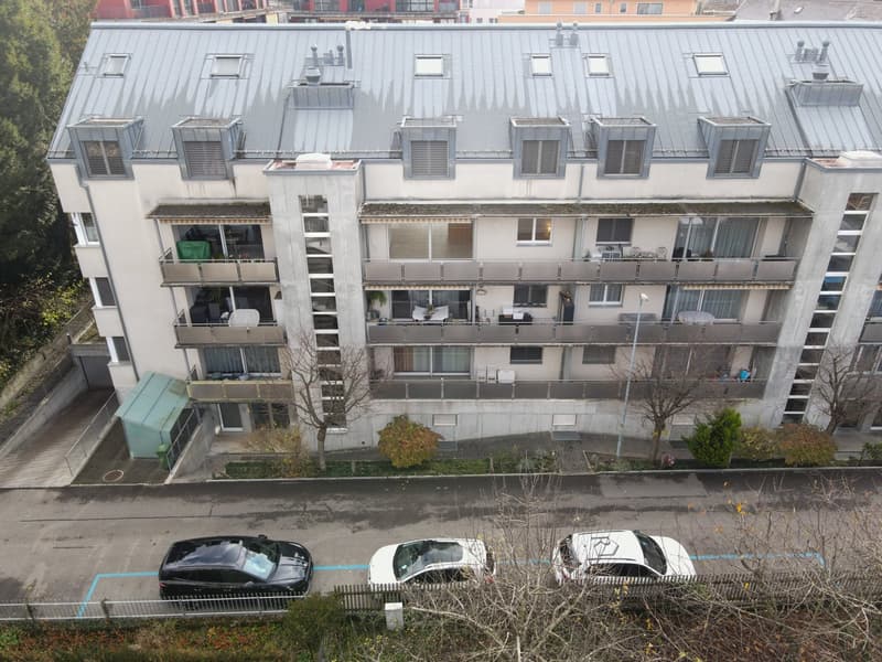 Multiple balconies, multiple windows, multiple cars parked in front