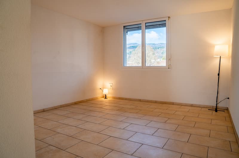 An empty room with white walls and wooden floor, a window with a view, two lamps, and a white power outlet.