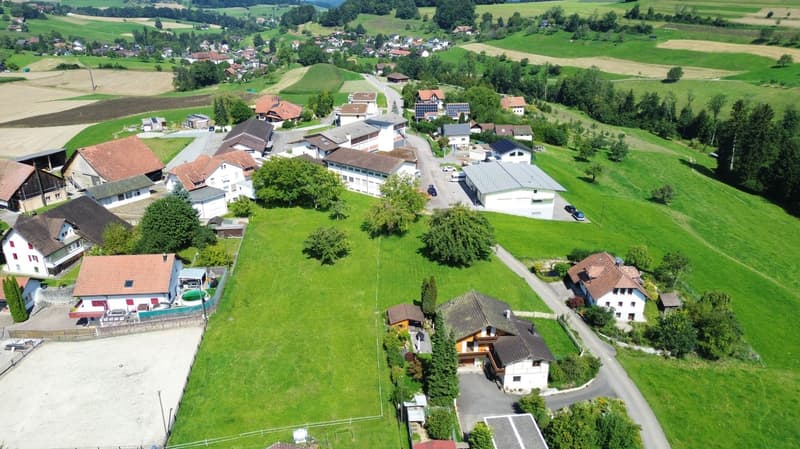 Residential homes with solar panels, driveways, lush green lawns, surrounded by agricultural fields and mountains in the background.