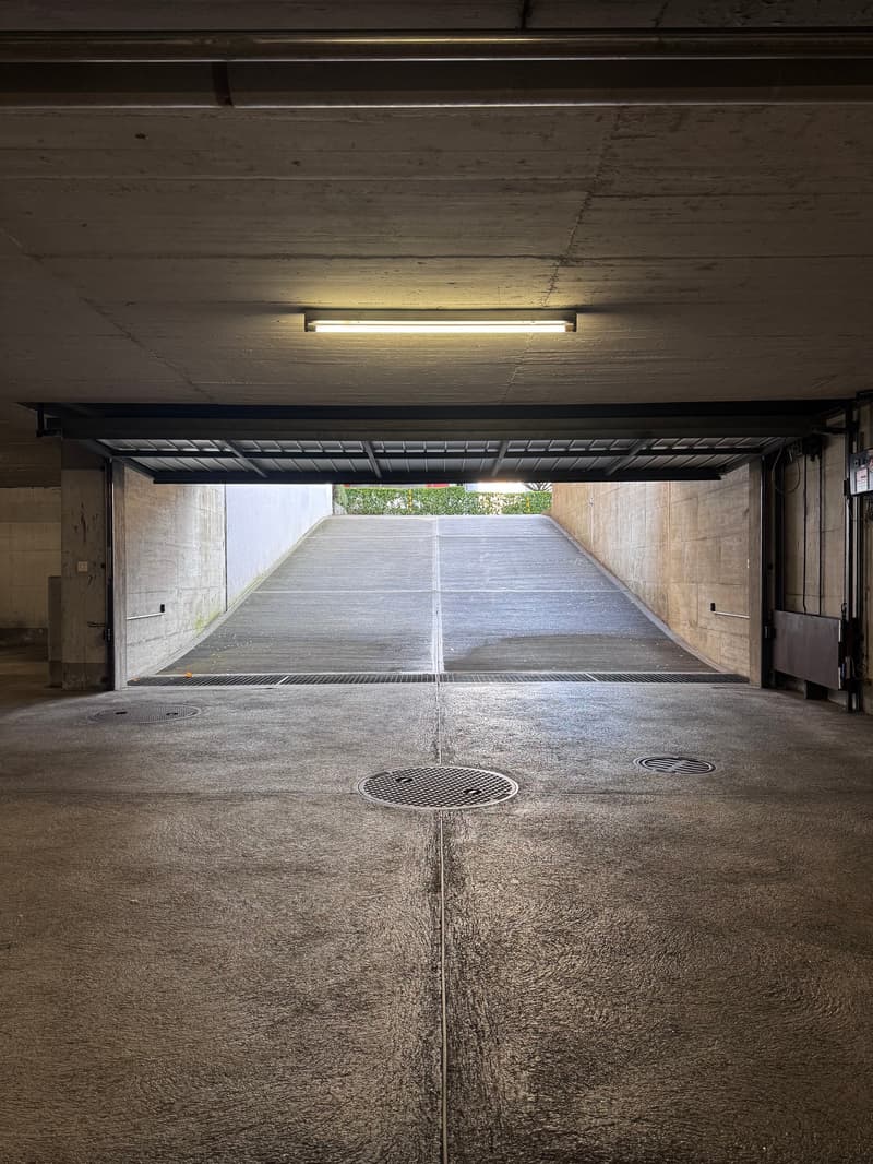 Empty underground garage with concrete walls, open ceiling, and an open space at the top end leading to outdoor.