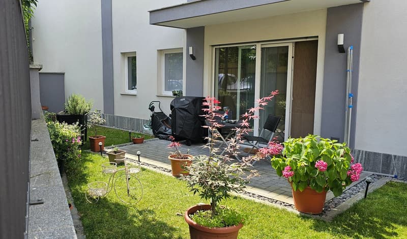 A small garden with a patio, various potted plants, a small table, and chairs.