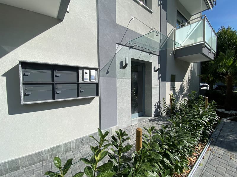 Modern building with gray walls, glass door, glass balcony, mailbox, and plants
