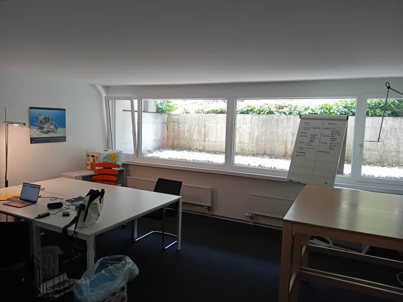 Office room with white walls, large windows, desks, chairs, radiators, whiteboard, picture, lamp, laptop, bags