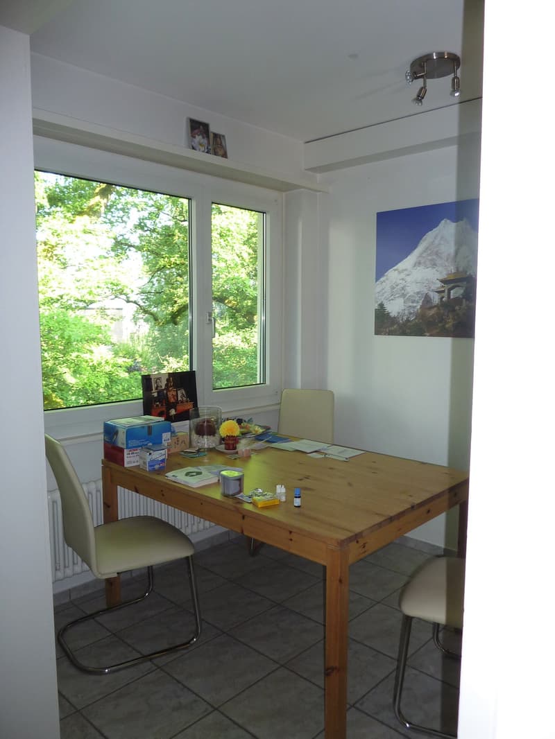 A room with a wooden desk, two chairs, a radiator, and a window with a view of trees outside.
