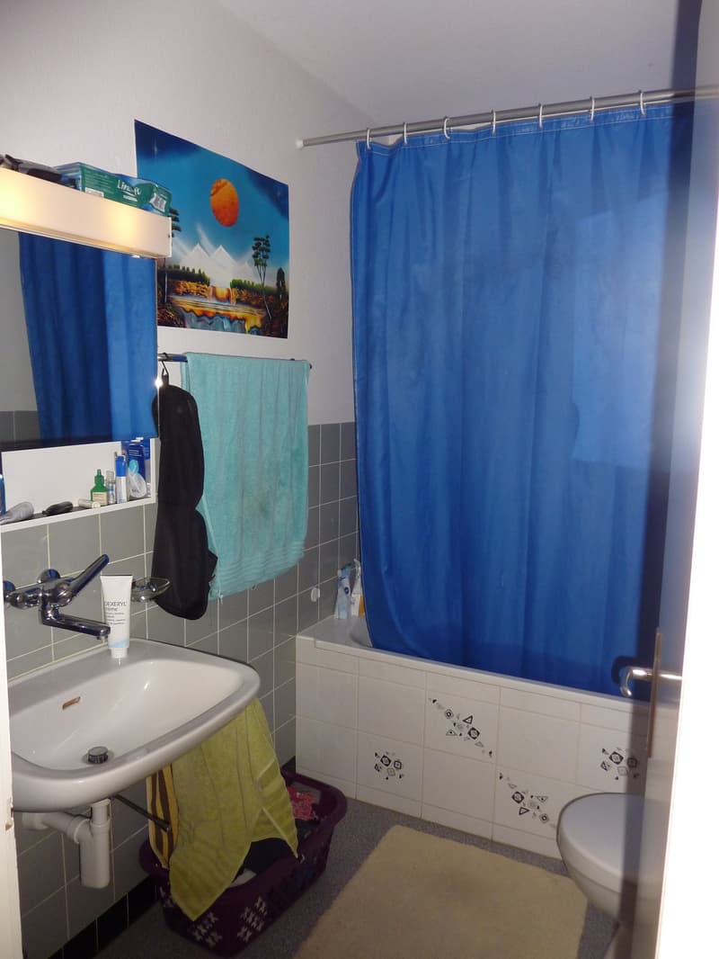 Bathroom with white sink, blue shower curtain, white bathtub, white toilet, tiled walls, towel rack, mirror, and storage basket.