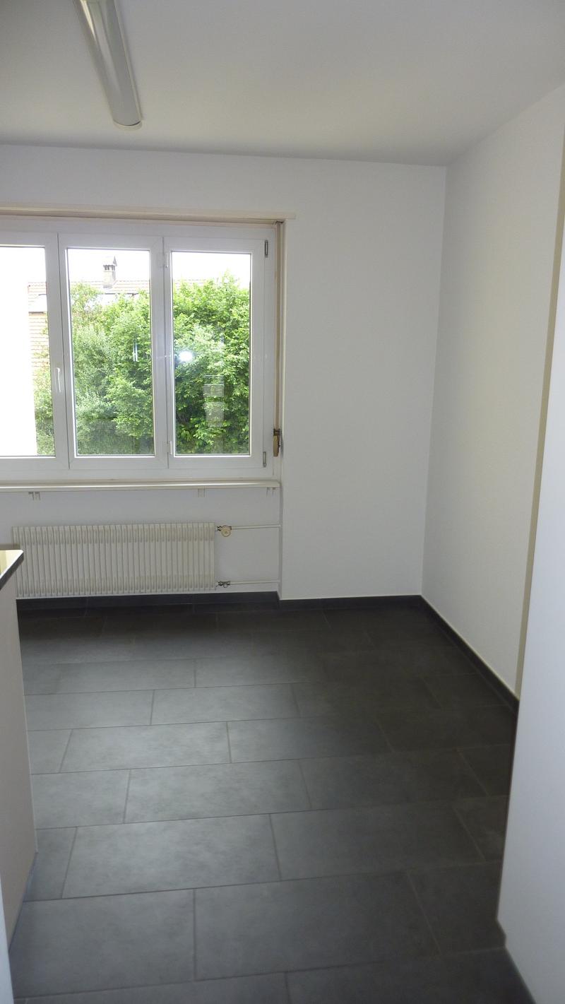 Empty room with white walls, black tiles, large window, white radiator