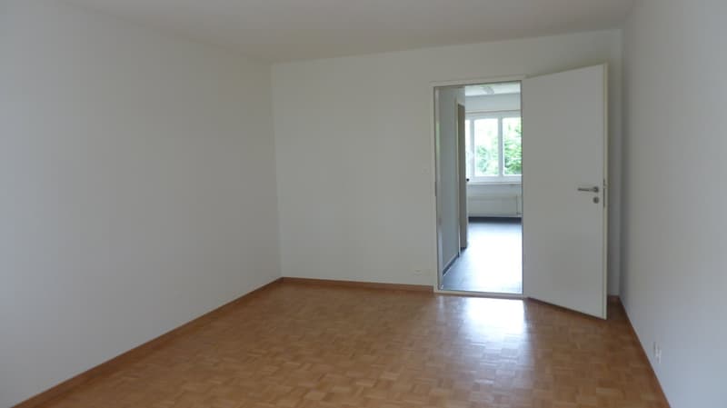 Empty room with wooden floor, white walls, open door, and window