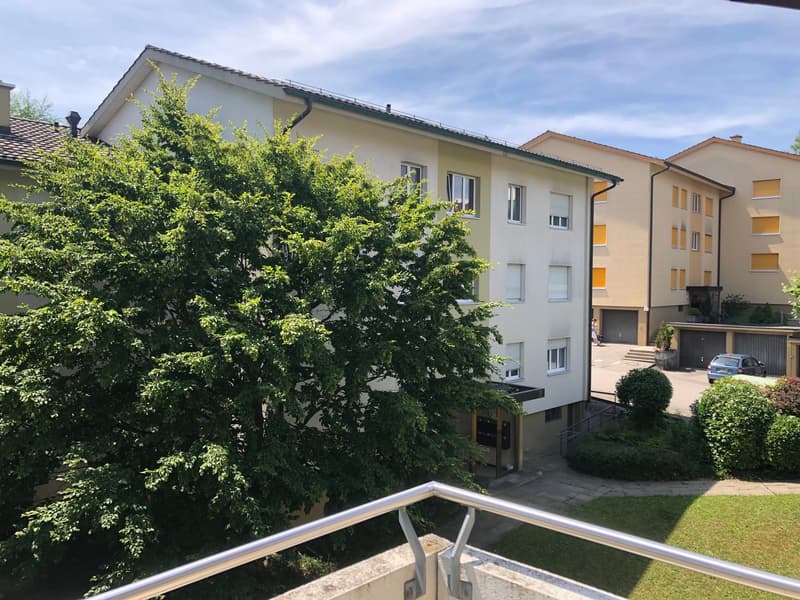 3 story building, white exterior, multiple windows, tree in front, balcony, garage