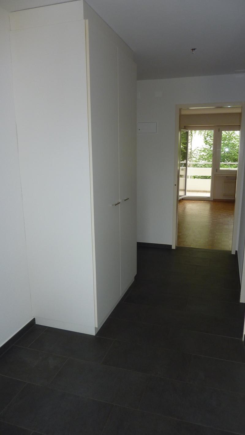 Empty room with white walls, black tiled floor, large white wardrobe, open door to balcony