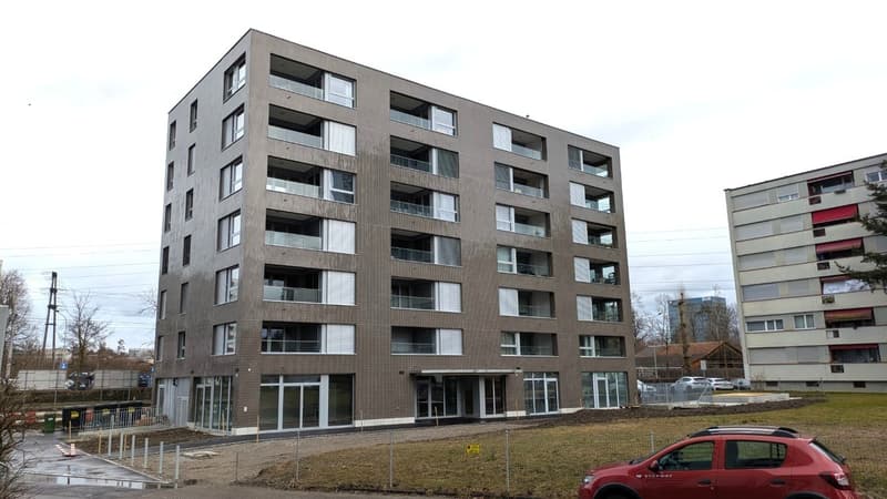 Modern building, brown brick, several balconies, large windows, ground floor entrance, underground parking