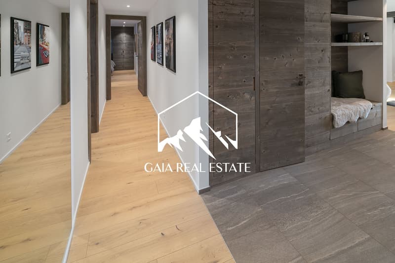 Spacious apartment with hardwood floors, white walls, and rustic wood paneling. The hallway leads to a bedroom with a built-in bed and shelving. The apartment features a fireplace and modern decor.