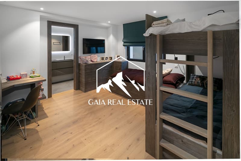 The image shows a bedroom with a bunk bed, wooden furniture, and a TV on the wall. The room has a modern and cozy design with neutral colors and wooden accents.