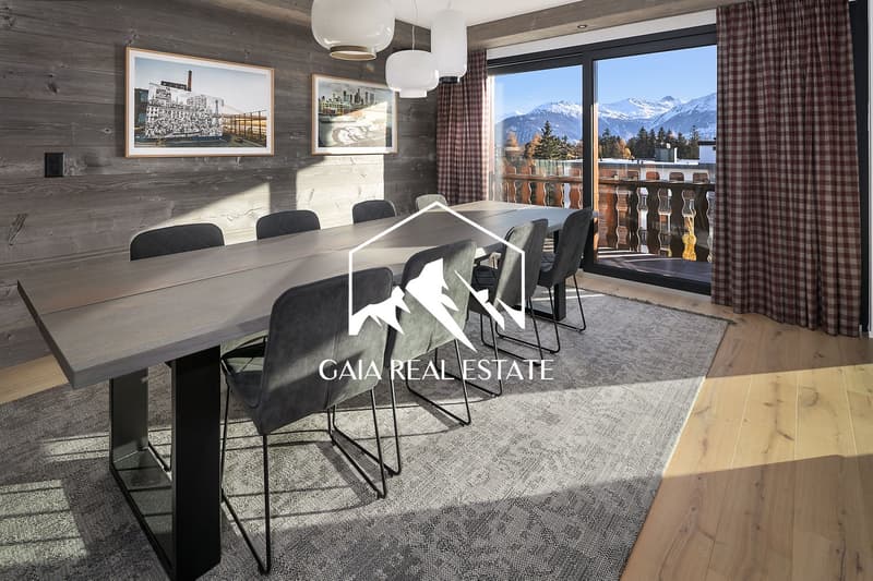 Spacious dining area with a large wooden table and black chairs, framed artwork on the walls, and a balcony with a scenic mountain view