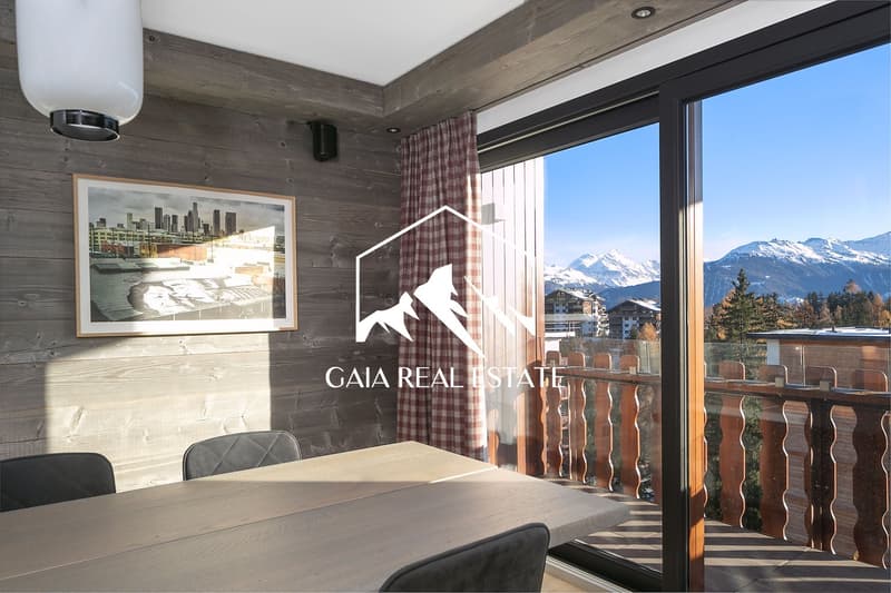 Rustic wooden walls, large windows with mountain view, dining table, chairs, framed artwork on the wall
