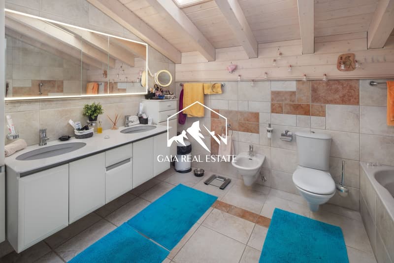 modern bathroom with double sink, toilet, bidet, bathtub, wooden ceiling, tiled floor, blue rugs