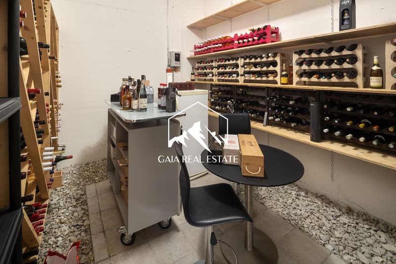 Wine cellar with wooden shelves, wine bottles, a table, and a chair.