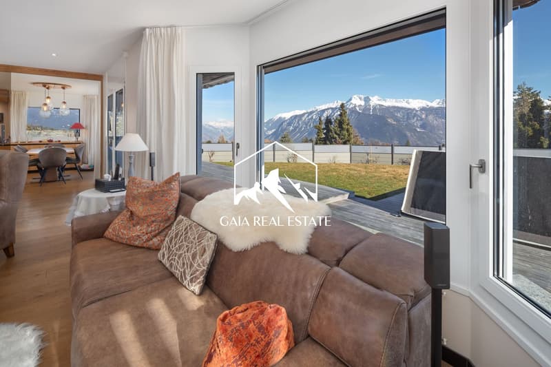 large windows, brown couch, white curtains, wooden floor, table, lamp, view of mountains