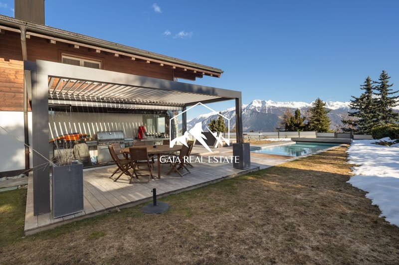 Modern house with wooden exterior, covered patio with dining area, swimming pool, and mountain view