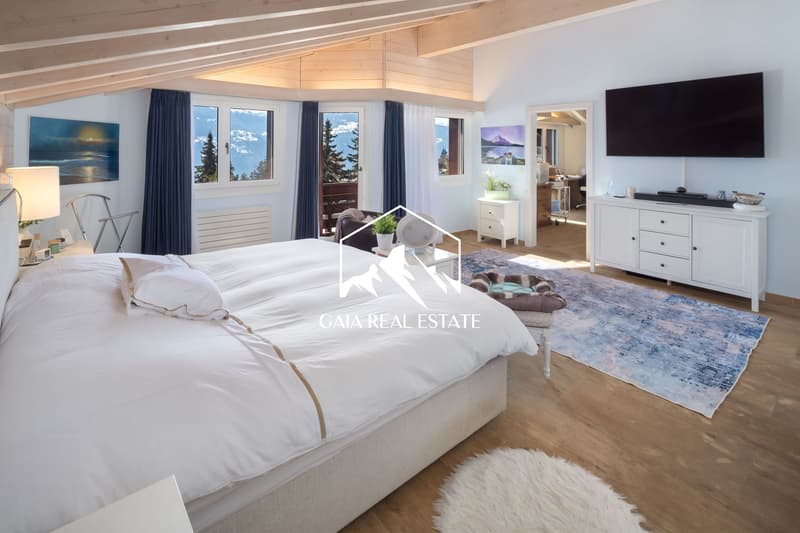 bedroom with a large bed, wooden floor, white walls, large windows, TV, rug, side table, lamp, painting, wooden ceiling