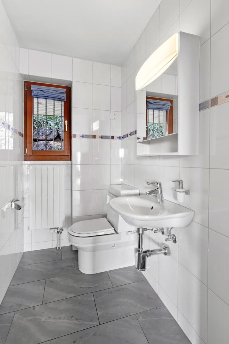 white tiled walls, gray tiled floor, white sink, toilet, window, radiator