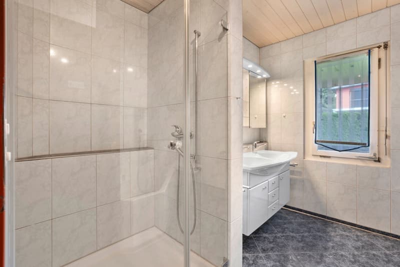 Modern bathroom with a shower, sink, and mirror. Tiled walls and floor.