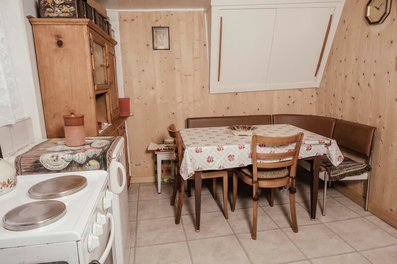 White stove, vintage wooden table and chairs, wooden bench, tiled floor, wooden cabinets, small wooden desk.