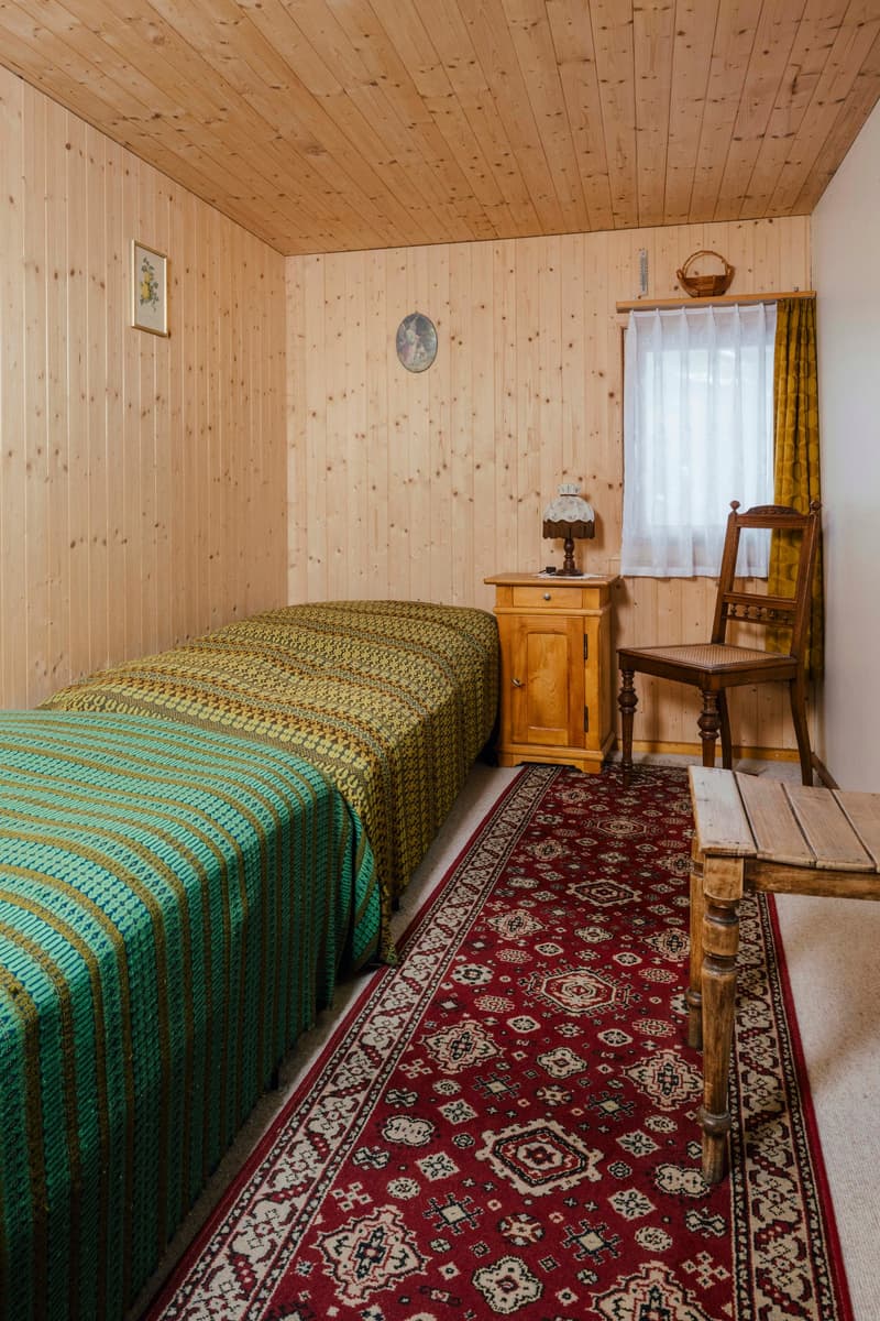 wooden walls, double bed, nightstand, chair, red carpet, rug, picture frame, lamp, basket