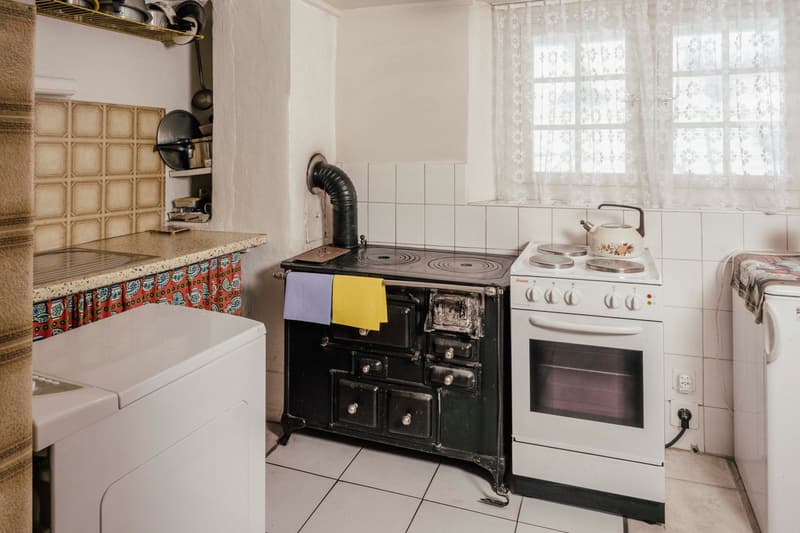 old kitchen with black stove, white oven, washing machine, and a window with curtains